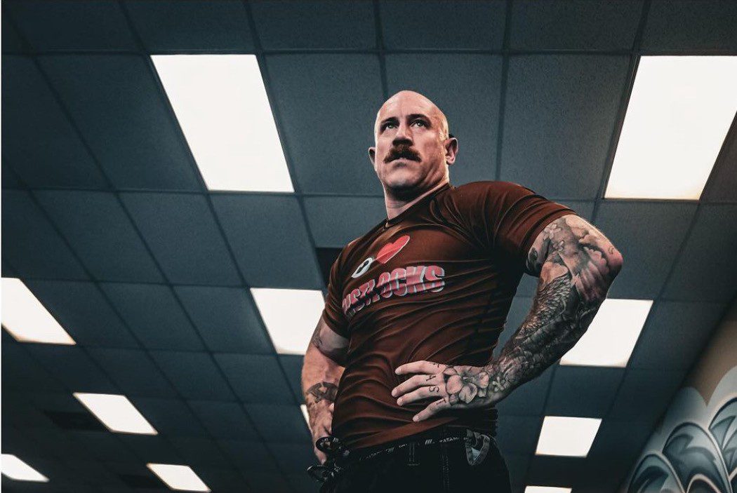 6836004ea6644_thumbnail_IMG_9747 A man with tattoos standing in an indoor setting.